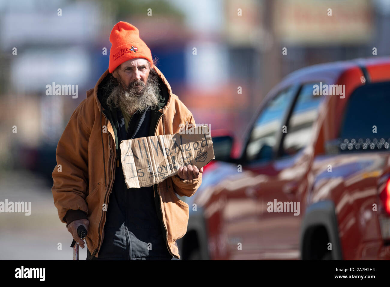 Homeless man panhandles for money at a busy intersection near a homeless encampment under a highway overpass days before a threatened crackdown by Texas Governor Greg Abbott on public right-of-way camping. Stock Photo
