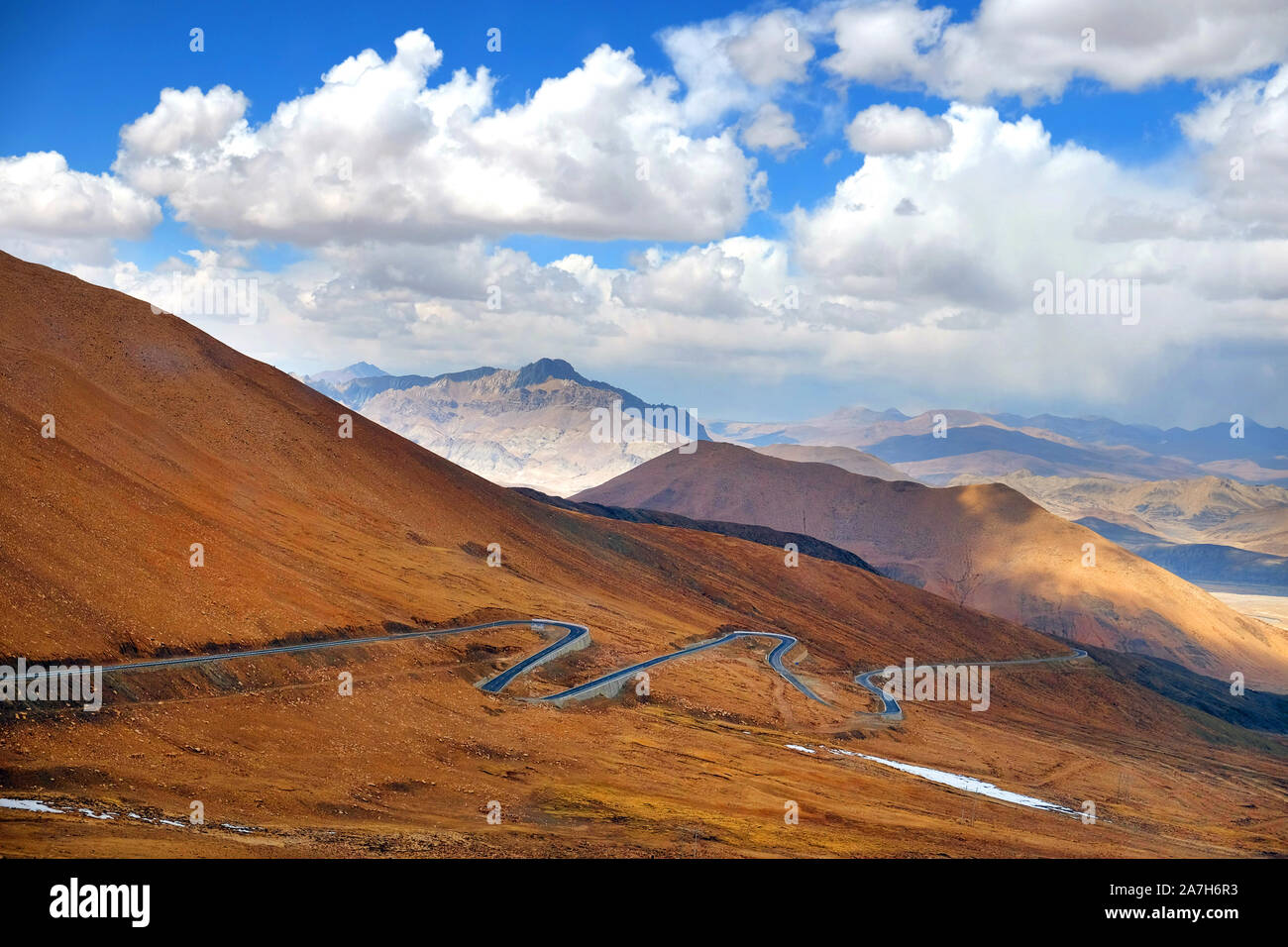 Highway stretching across the brown Himalaya Mountains, against a blue sky covered by white clouds. Stock Photo