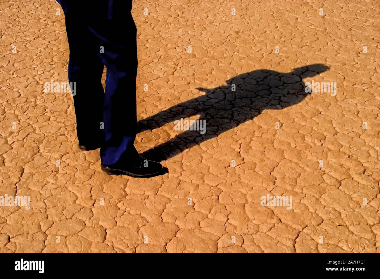 Man's legs in business slacks and full body shadow on cracked desert ground Stock Photo