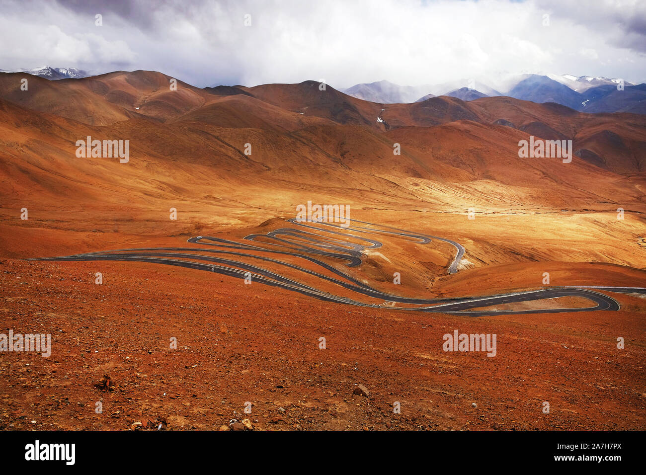 Highway stretching across the brown Himalaya Mountains, against a blue sky covered by white clouds. Stock Photo