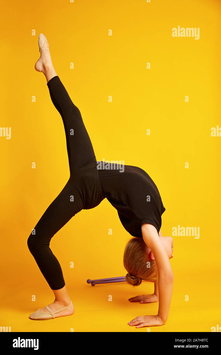 Little gymnast dancing acrobatic movements on yellow background, rhythmic gymnastics school, happy sportive childhood Stock Photo