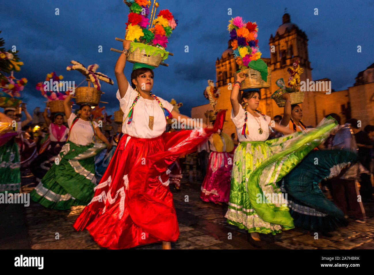 Young women dressed in traditional costumes perform the Flor de Pina dance in a comparsas past the Santo Domingo de Guzmán Church during the Day of the Dead Festival known in Spanish as Día de Muertos on November 2, 2013 in Oaxaca, Mexico. Stock Photo