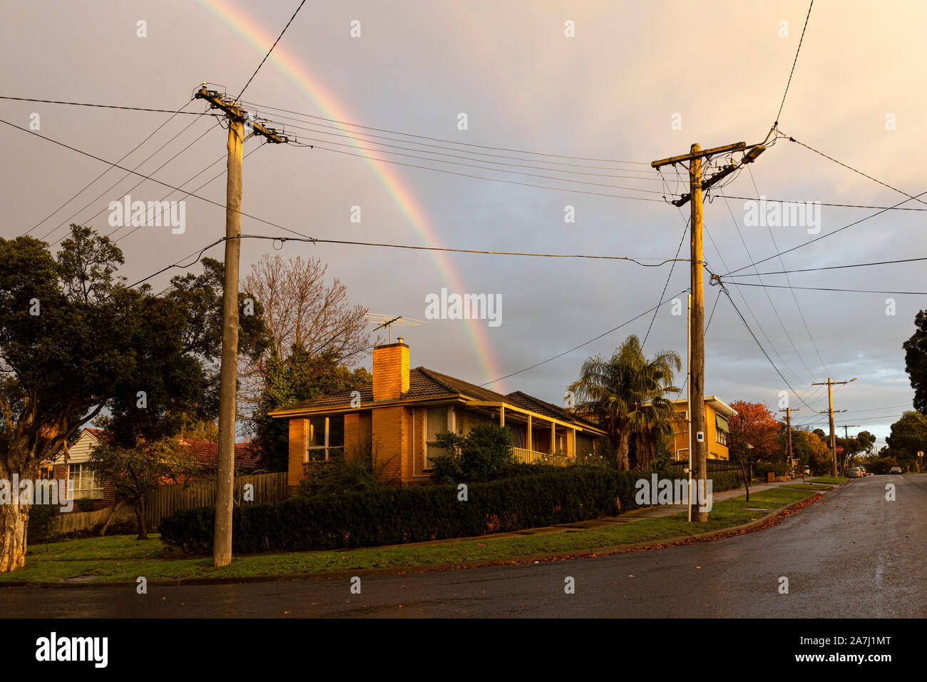 Suburban area street with rainbow pointing straight through frames center. Stock Photo
