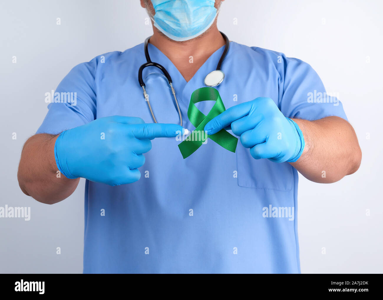 doctor in blue uniform and latex gloves holds a green ribbon as a symbol of early research and disease control, symbol of Lyme disease, kidney transpl Stock Photo