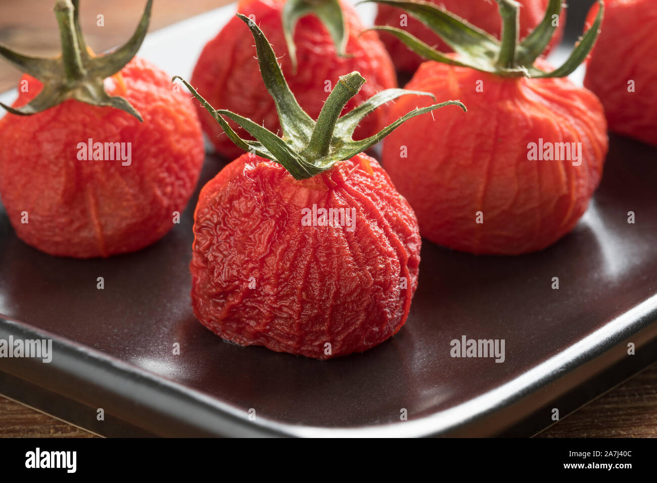 Roasted peeled red vine tomatoes with stem on a dish close up Stock Photo Alamy