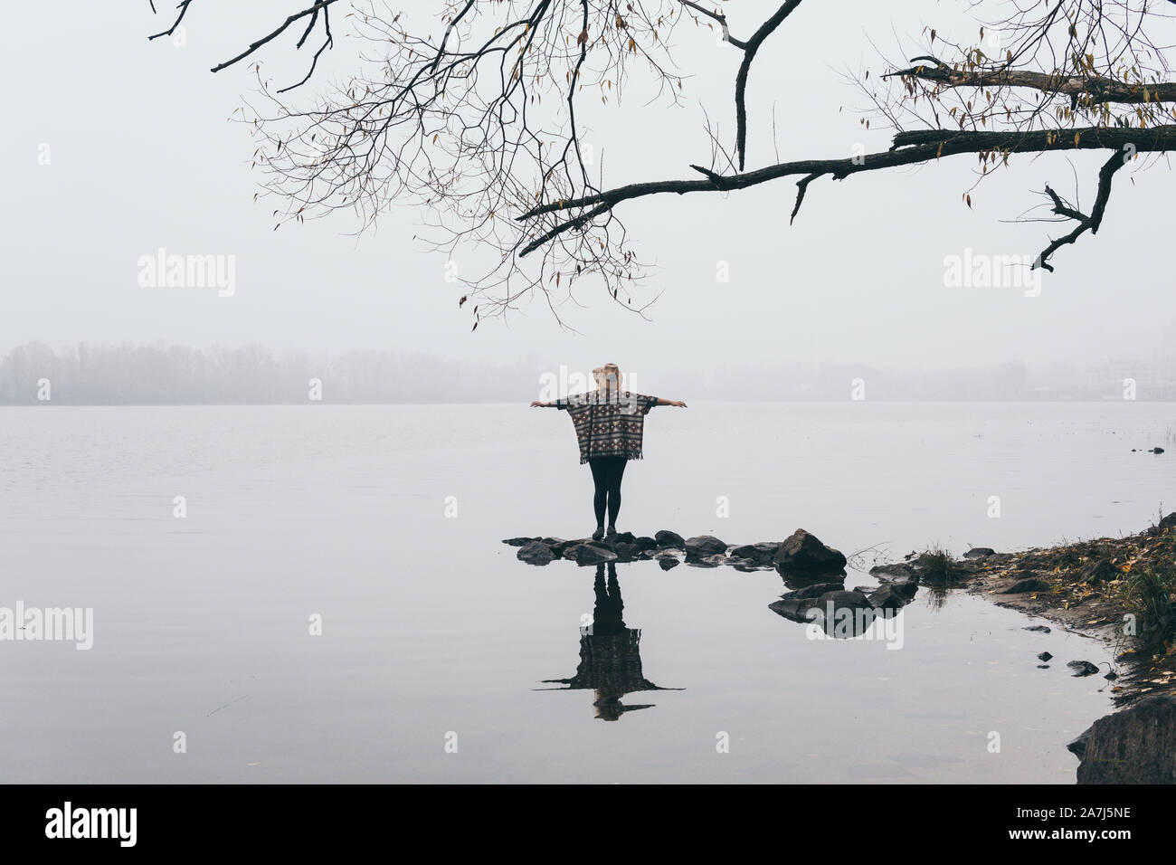Woman silhouette standing on the river bank in the morning fog with hands lifted up Stock Photo