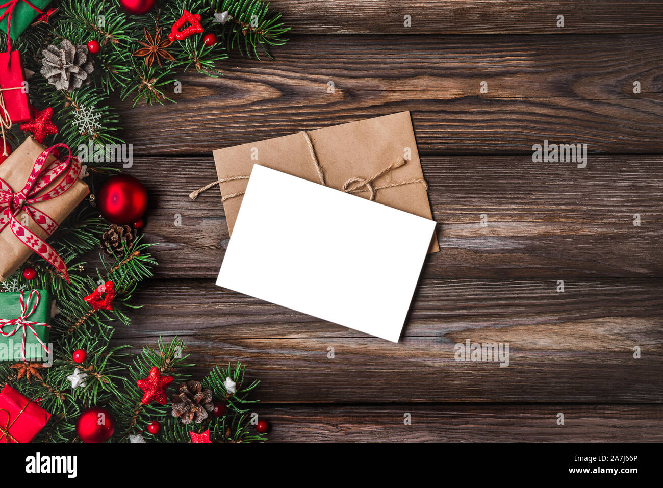 Christmas and Happy New Year greeting card with fir tree branches, gift boxes, red holiday decorations on rustic wooden table. mock up. top view with Stock Photo