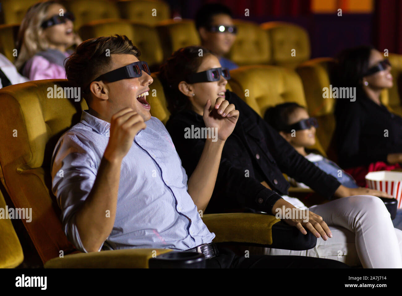 Amazed young man and woman couple in 3D glasses sitting on comfortable chairs and watching exciting film in movie theater being on date Stock Photo