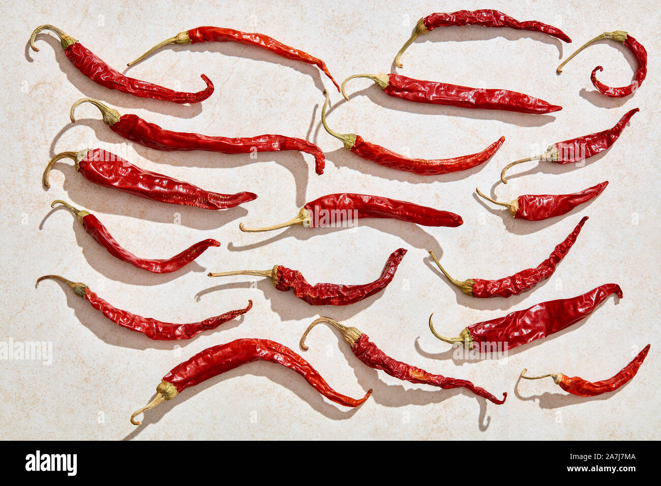 Sun dried red hot chili peppers under harsh sunlight with white stone background. Top view Stock Photo