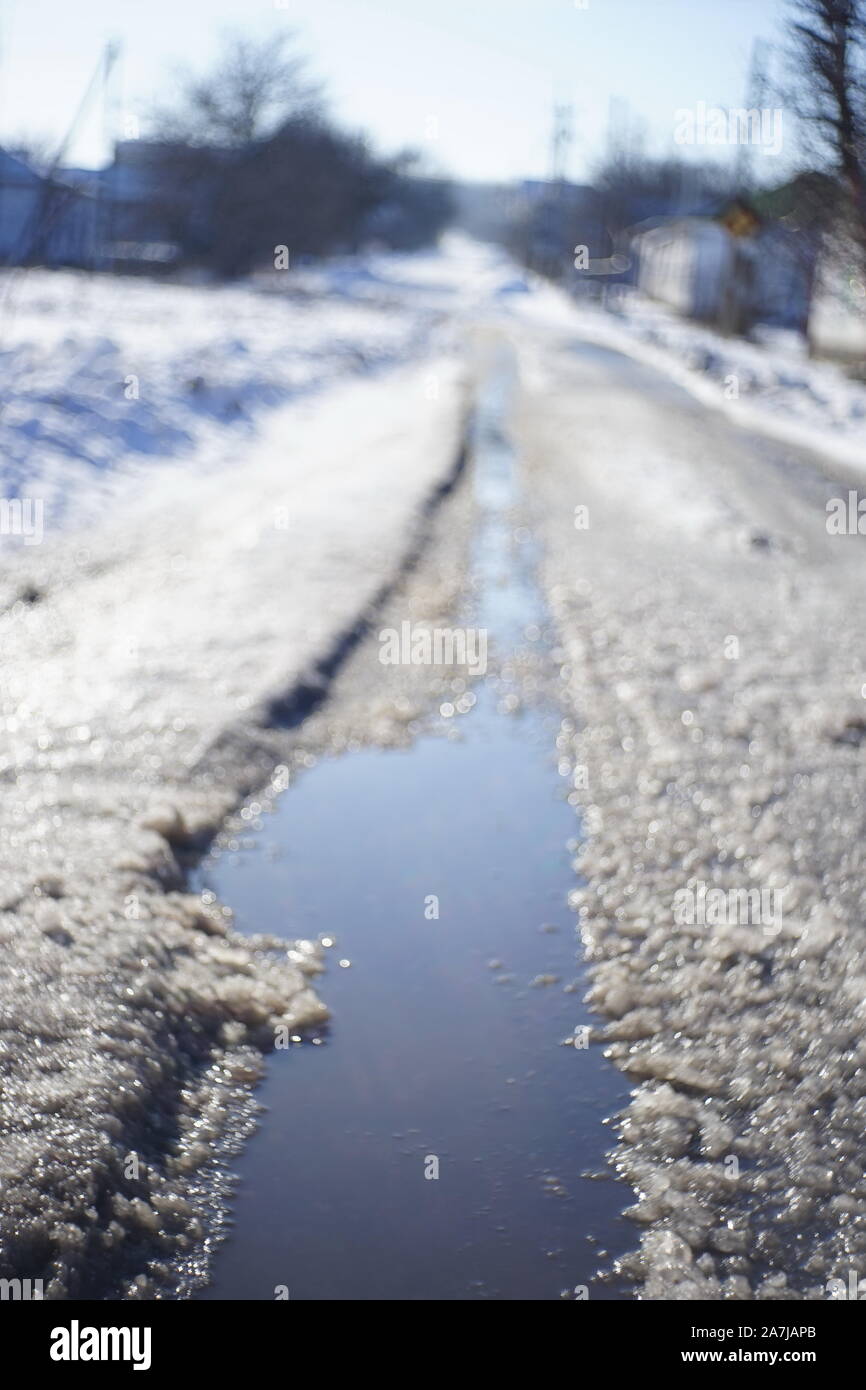 Difficult weather conditions. Winter sleet. Rural road in the snow with a puddle. Stock Photo