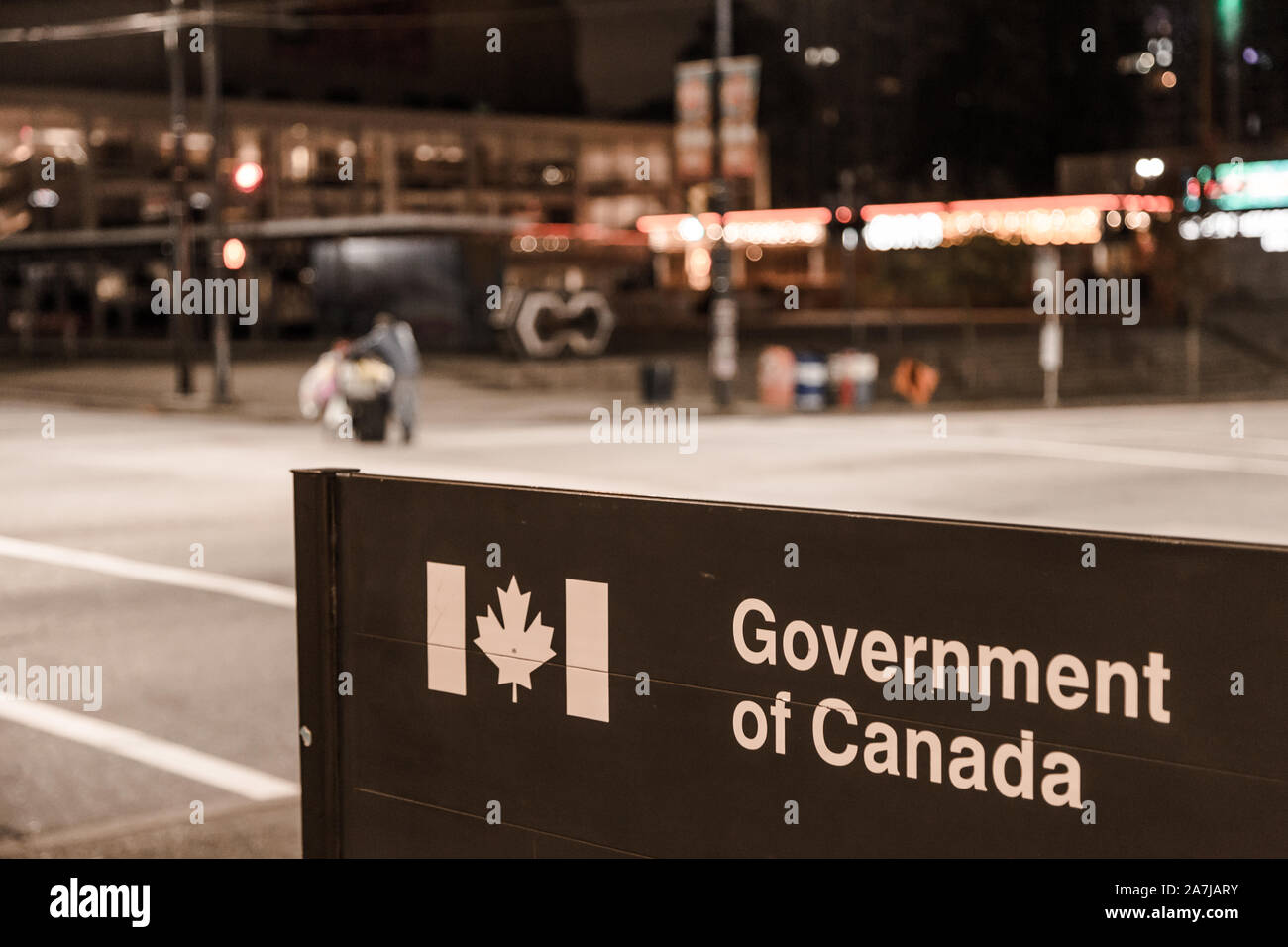 VANCOUVER, BC, CANADA - OCT 05, 2019: A homeless man with a shopping cart, out of focus, passing by a Government of Canada, subject of focus, federal Stock Photo