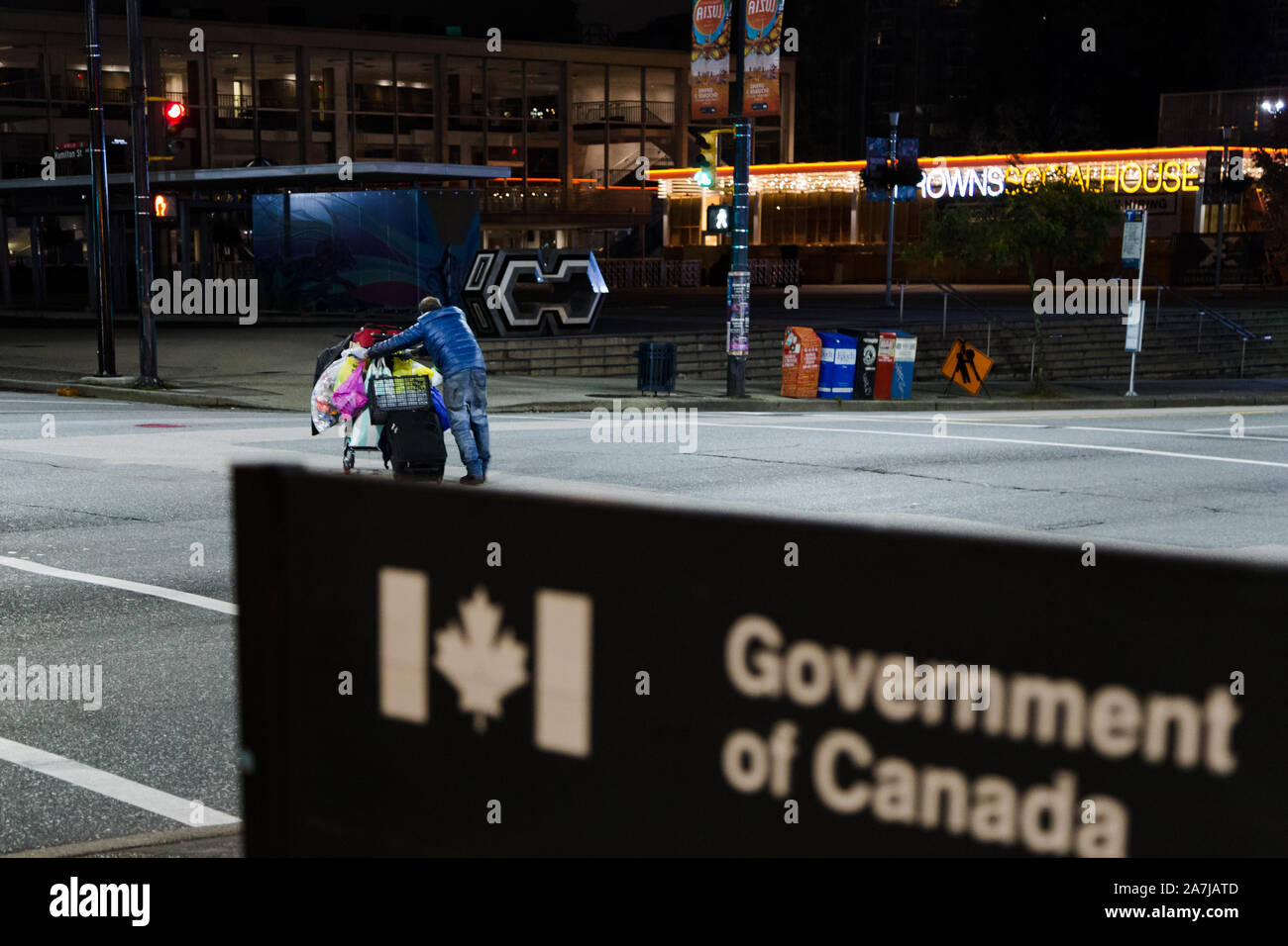 VANCOUVER, BC, CANADA - OCT 05, 2019: A homeless man with a shopping cart as the subject of focus passing by a Government of Canada, out of focus Stock Photo