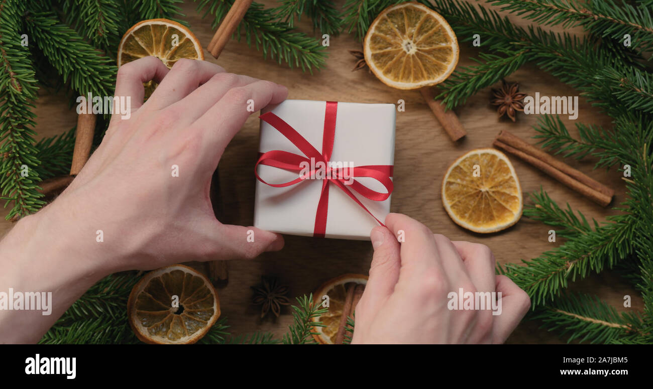Top view man hand untie red ribbon bow on gift box on decorated oak table, wide photo Stock