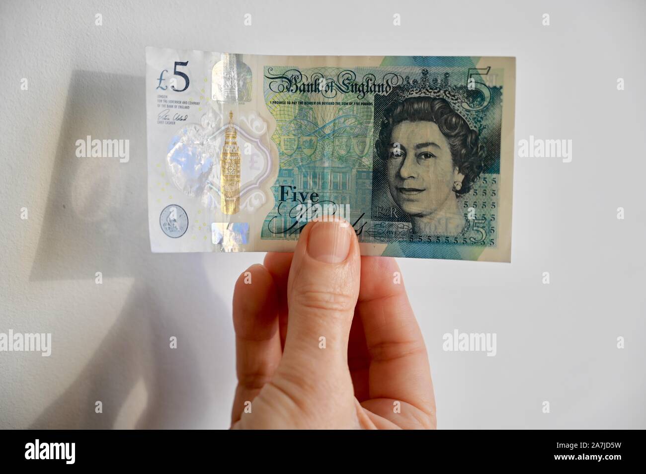 Close up of senior women holding a five pounds polymer sterling note. Stock Photo