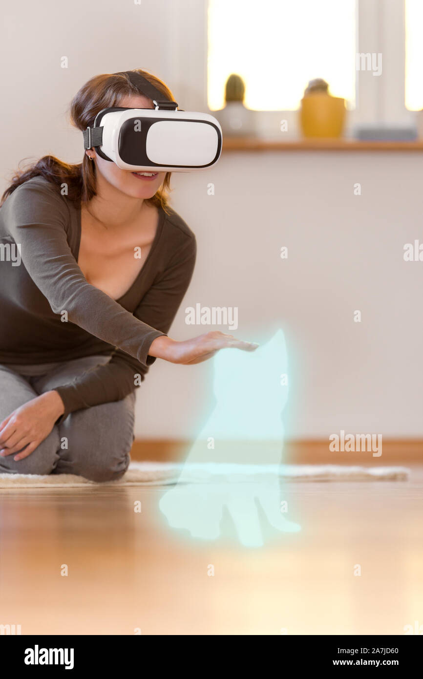 woman is stroking an dog hologram, wearing virtual reality glasses Stock Photo