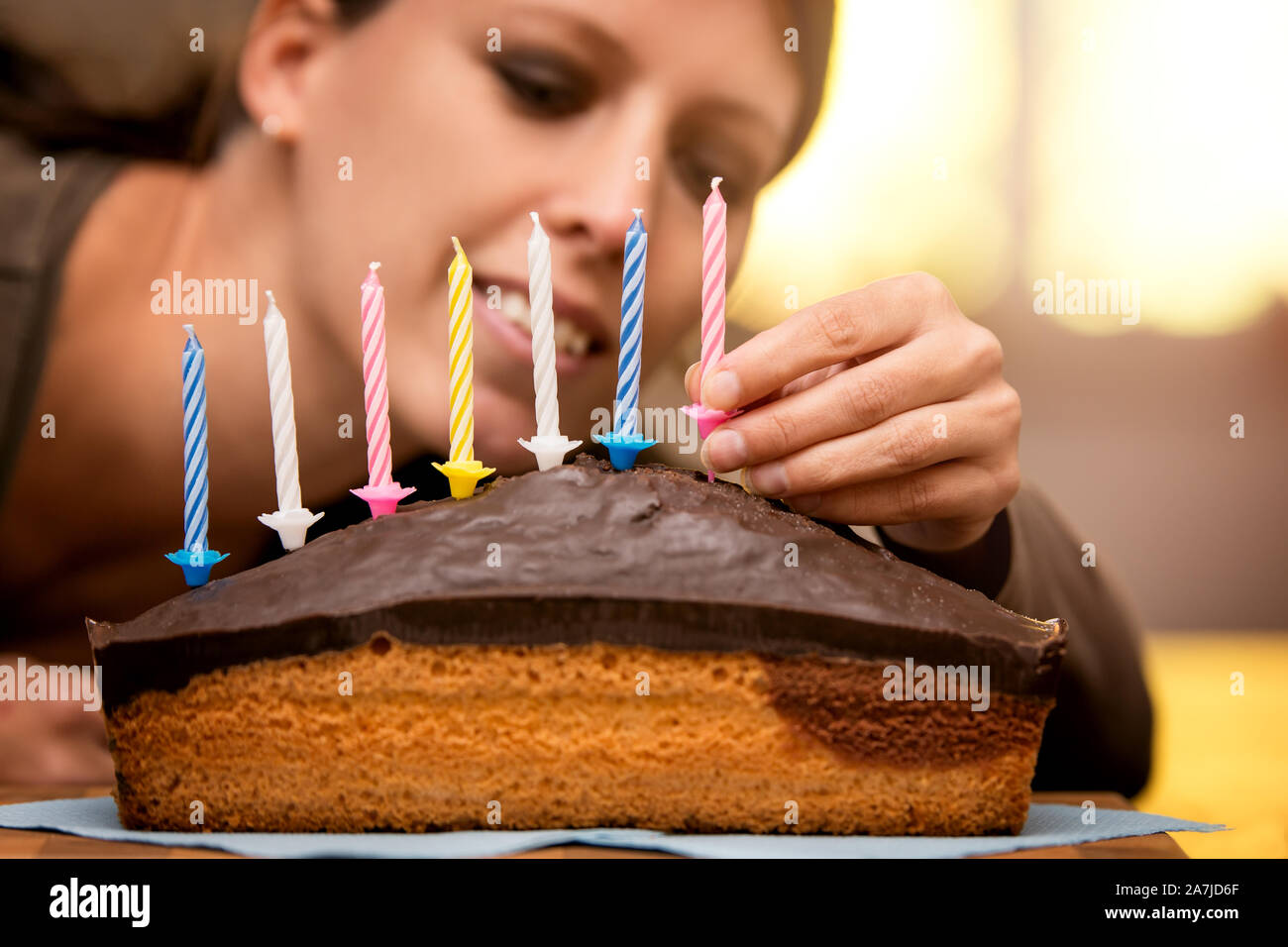pretty woman is decorating a marble cake with colorful candles Stock Photo