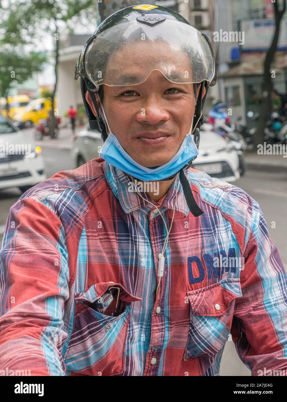 Horizontal portrait of young grinning male scooter driver wearing colorful red and blue checked shirt, black helmet with clear plastic visor. Stock Photo