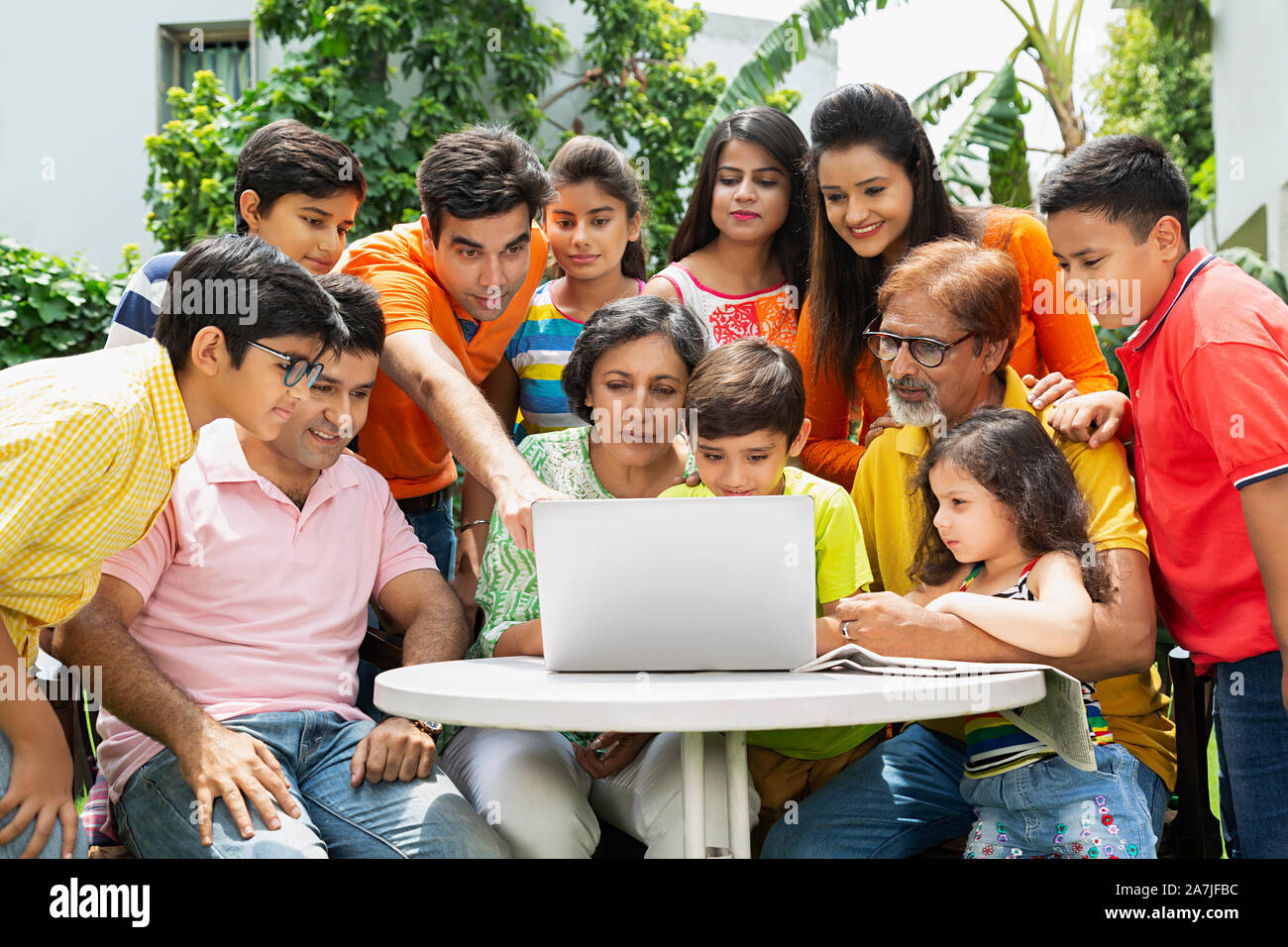 Group-of Three Generation Family Looking-at laptop Screen And Pointing finger in-Courtyard Of their House Stock Photo