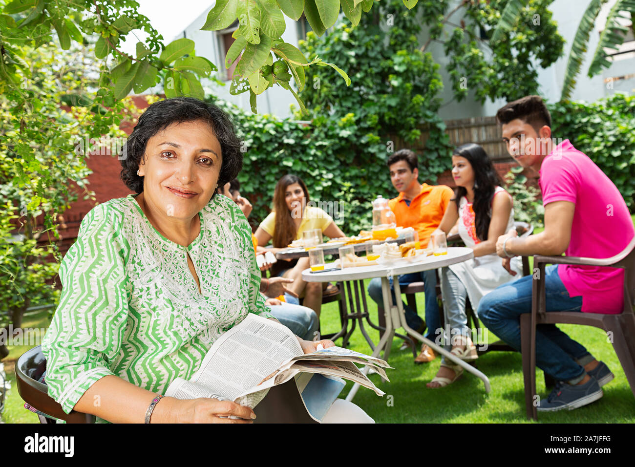 Happy indian Family Eating Breakfast Together in the house courtyard And Senior Female Reading Newspaper in foreground Stock Photo