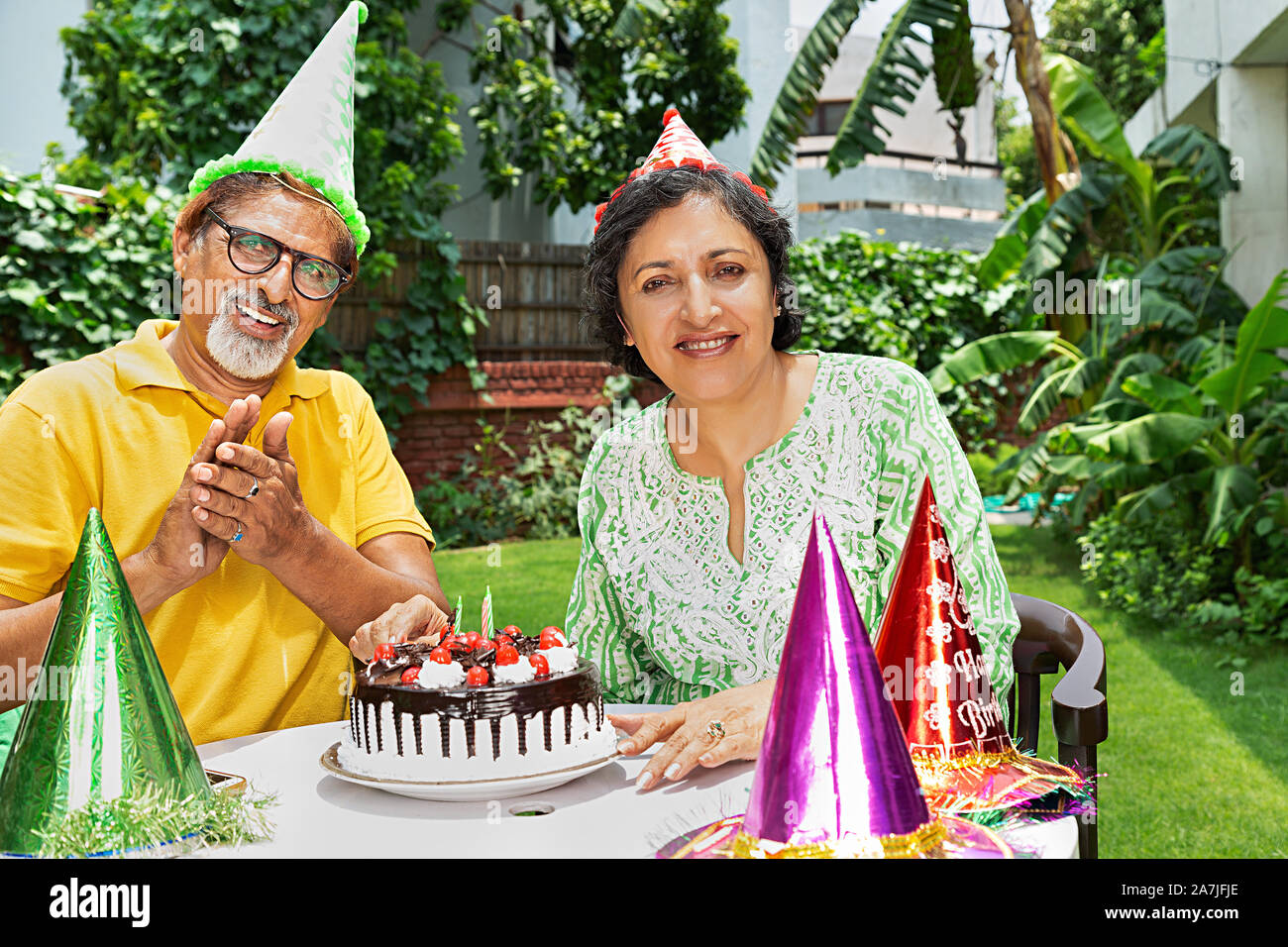 Happy Old couple celebrating birthday and cutting birthday cake at-courtyard of-their home Stock Photo