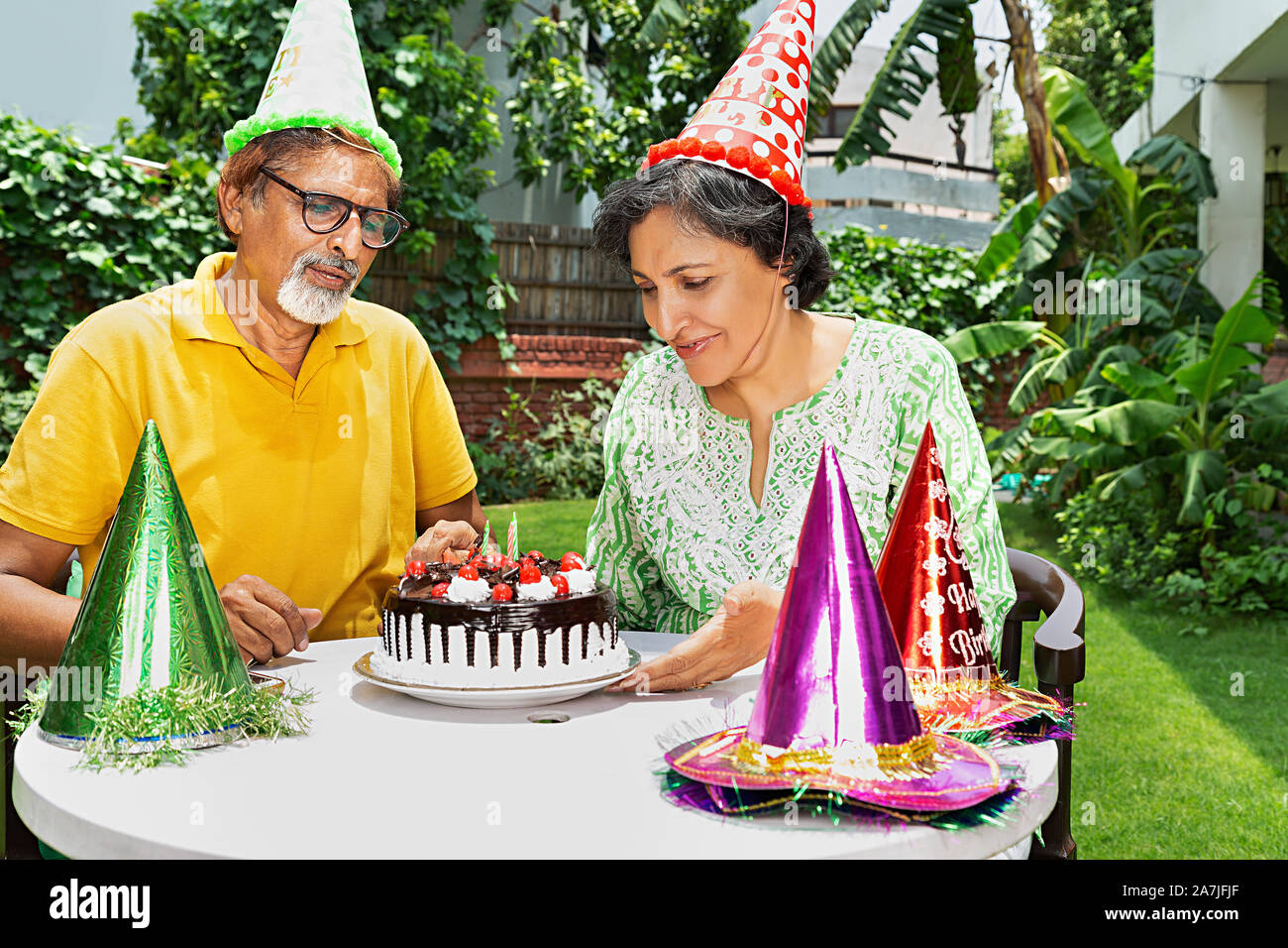 Happy Senior Couple cut their cake during a 55th anniversary celebration in-garden of-their house Stock Photo
