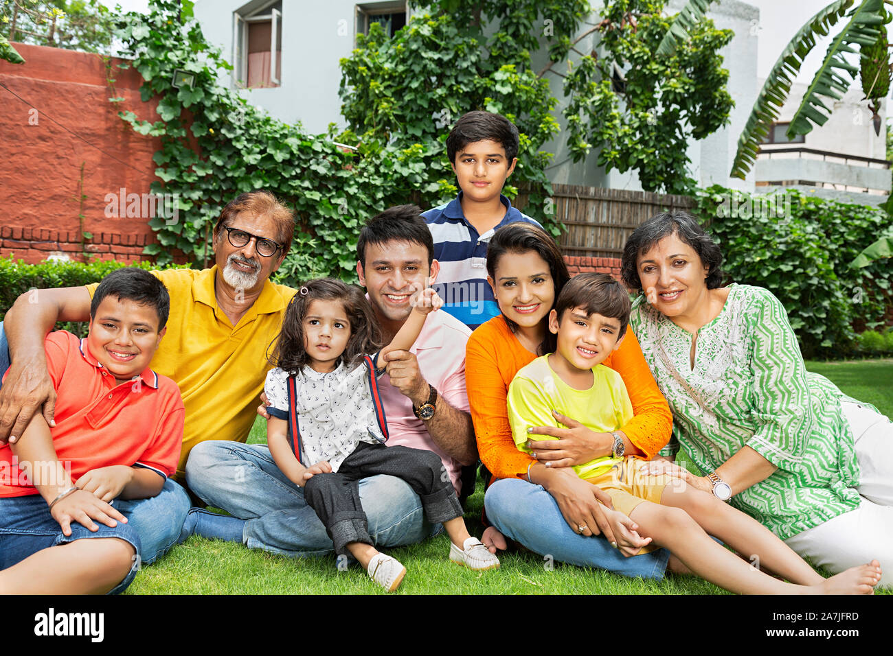Group of Indian family Grandparents, Parents and Children Sitting-on-grass relaxing Together in front of their home in the garden Stock Photo
