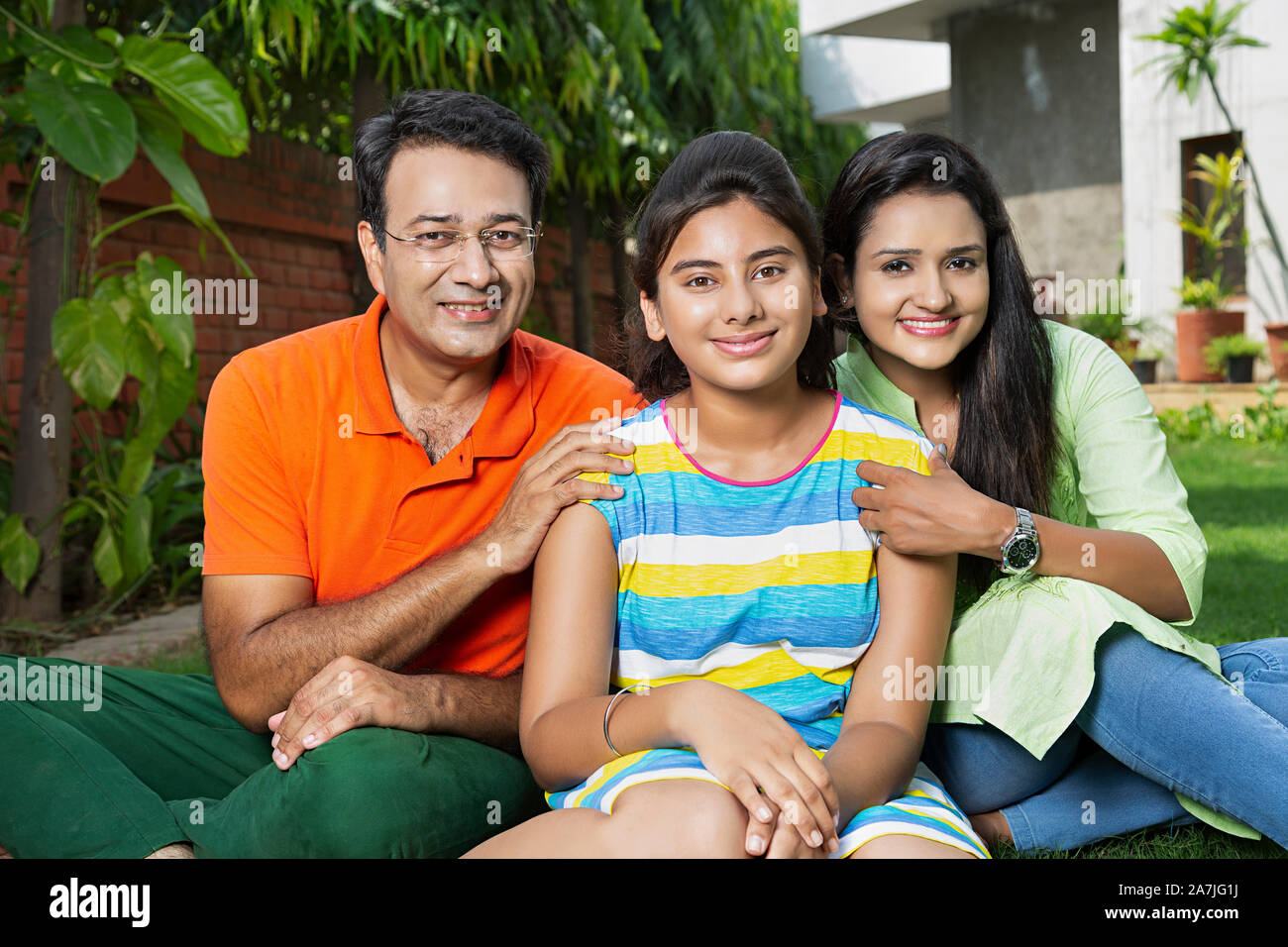 Happy Family Father And Mother With Teenager Girl sitting On grass And Relaxing in the courtyard of their house Stock Photo