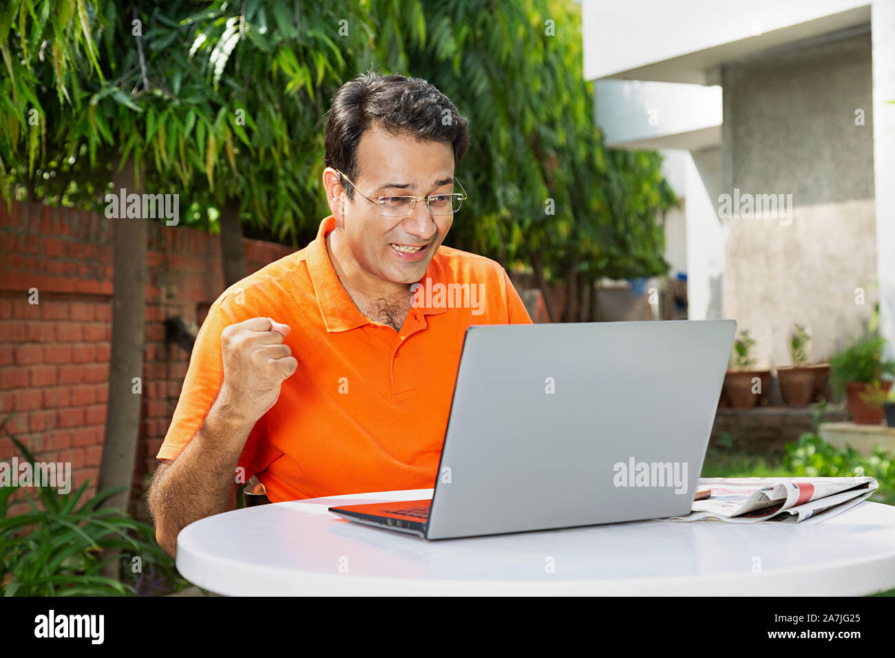 Happy Mid-adult male Looking-at laptop-Screen Fists-hand Winning Success Celebration in-Courtyard of their house Stock Photo