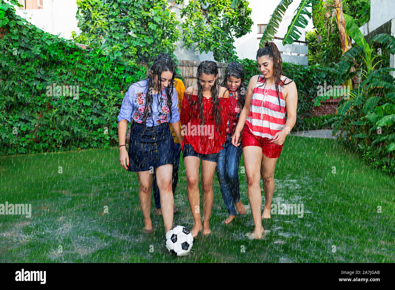 Group-Of Young Girls Friends Playing Soccer Ball game In-The Rain In-courtyard Of Their House Stock Photo