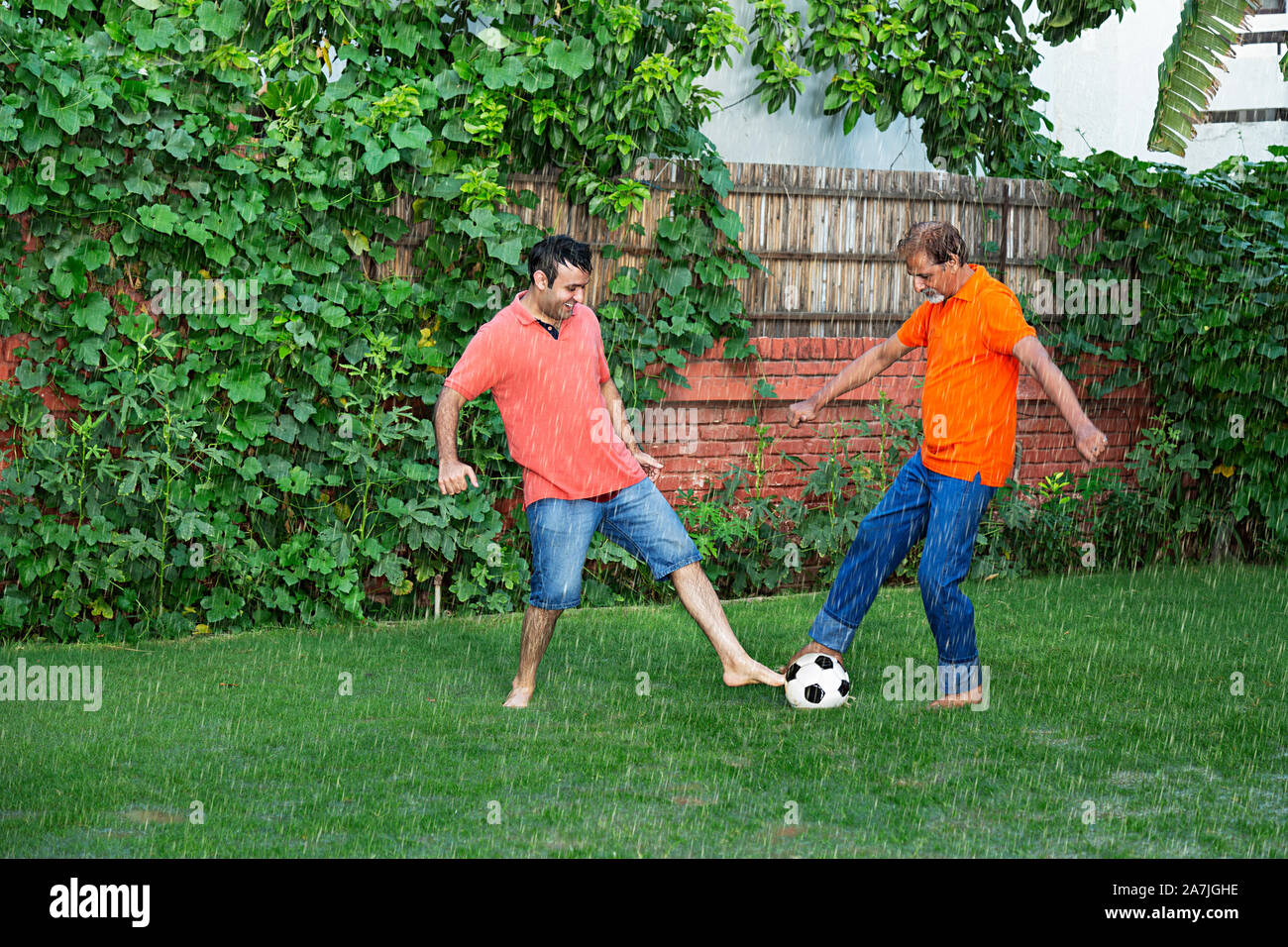 Happy indian Family Elderly Father and Adult-son playing Football game In-The Rain In-garden of-Their Home Stock Photo
