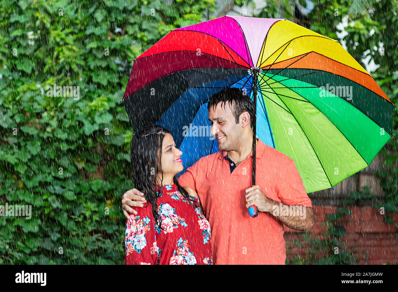 Happy Romantic Couple in-love under the umbrella Enjoying The Rain in-park on Summer season Stock Photo