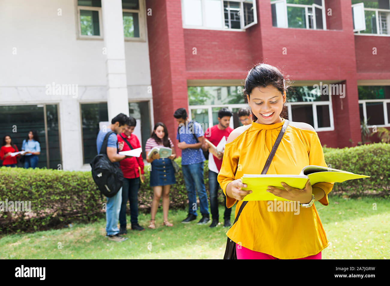 Teenager Girl College student reading book while friends standing in background at-college Campus Stock Photo