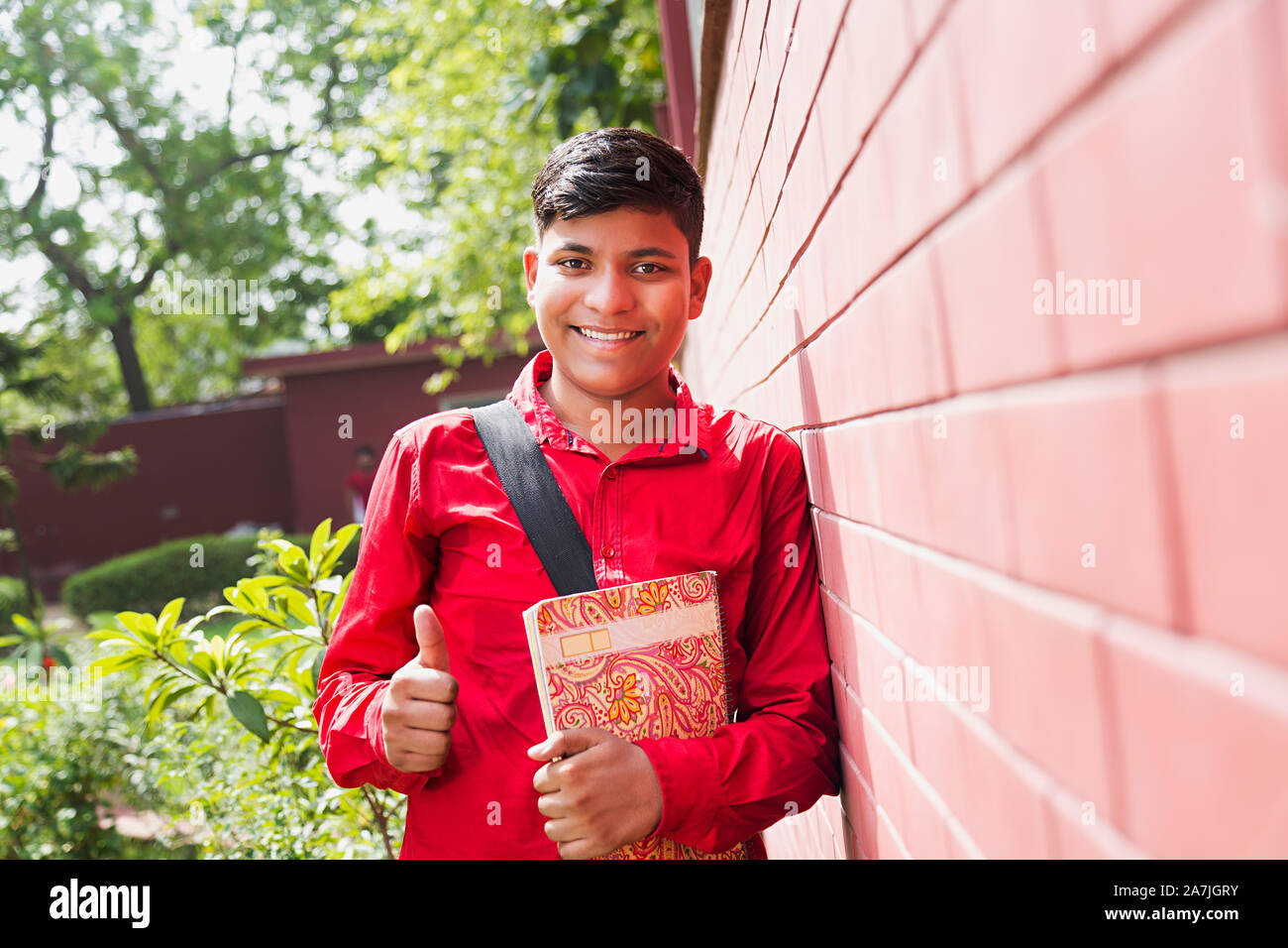 Young Teenage Boy College Student Holding Book While Showing Thumbs-up Outside College University Campus Stock Photo