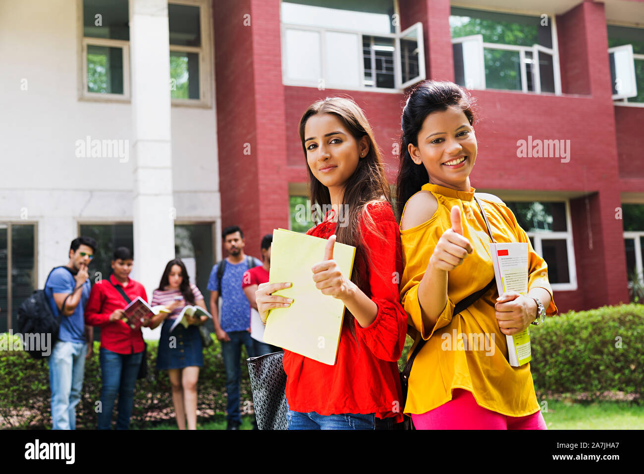 Two Young Teenager Girls College Student Classmate Standing back-to-back Holding book While Showing Thumbs-up At-Campus Stock Photo