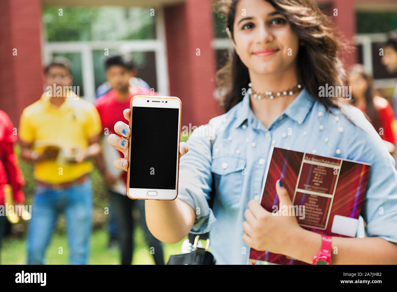 Close-up Young Female College student Showing Smart Phone Screen And People-In-The-background In-Outside Campus Stock Photo