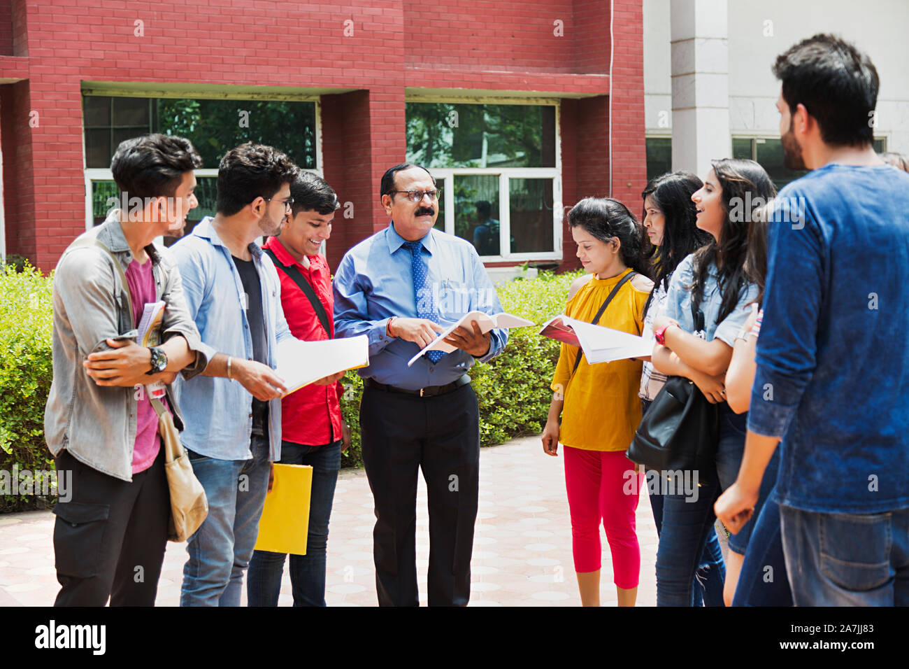 Group Of College Students Boys And Girls With Professor Studying Book Discussion Education