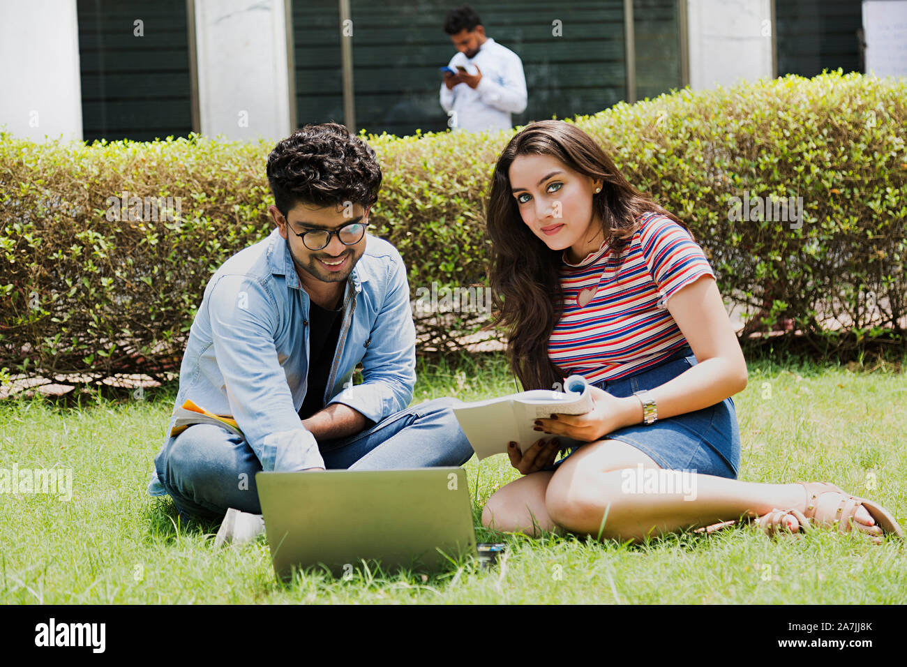 Two Young College Couple Students Studying Book With Laptop Education Learning Sitting-on-Grass At-Campus Stock Photo