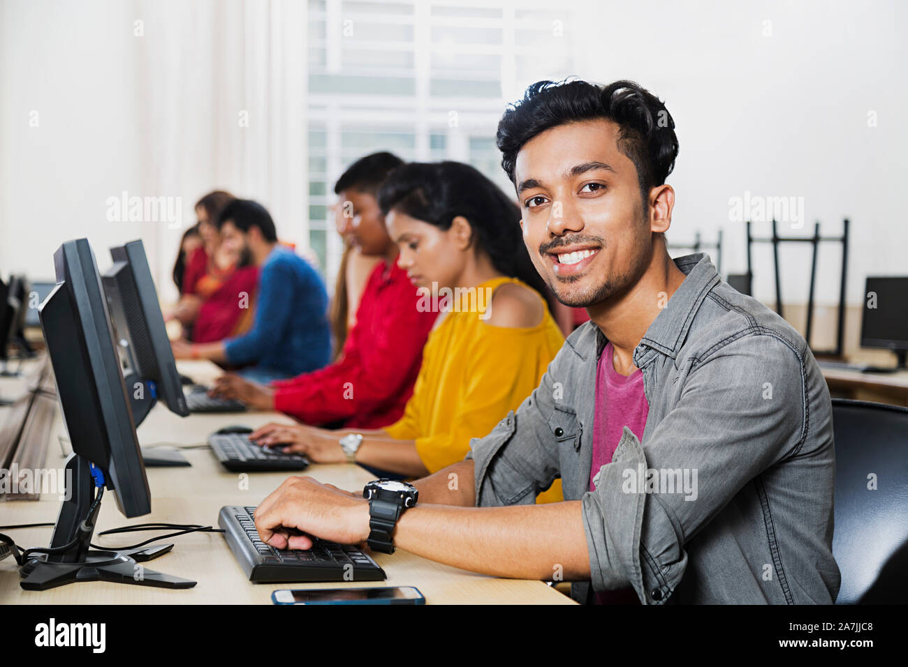 Young Male College Student Using Computer Studying E-Learning Education With Students In Computer Class Stock Photo