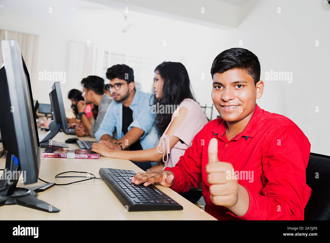 Indian College Boy-Student Using Computer Showing Thumb-up Studying E-Learning With Classmates At Computer Class Stock Photo