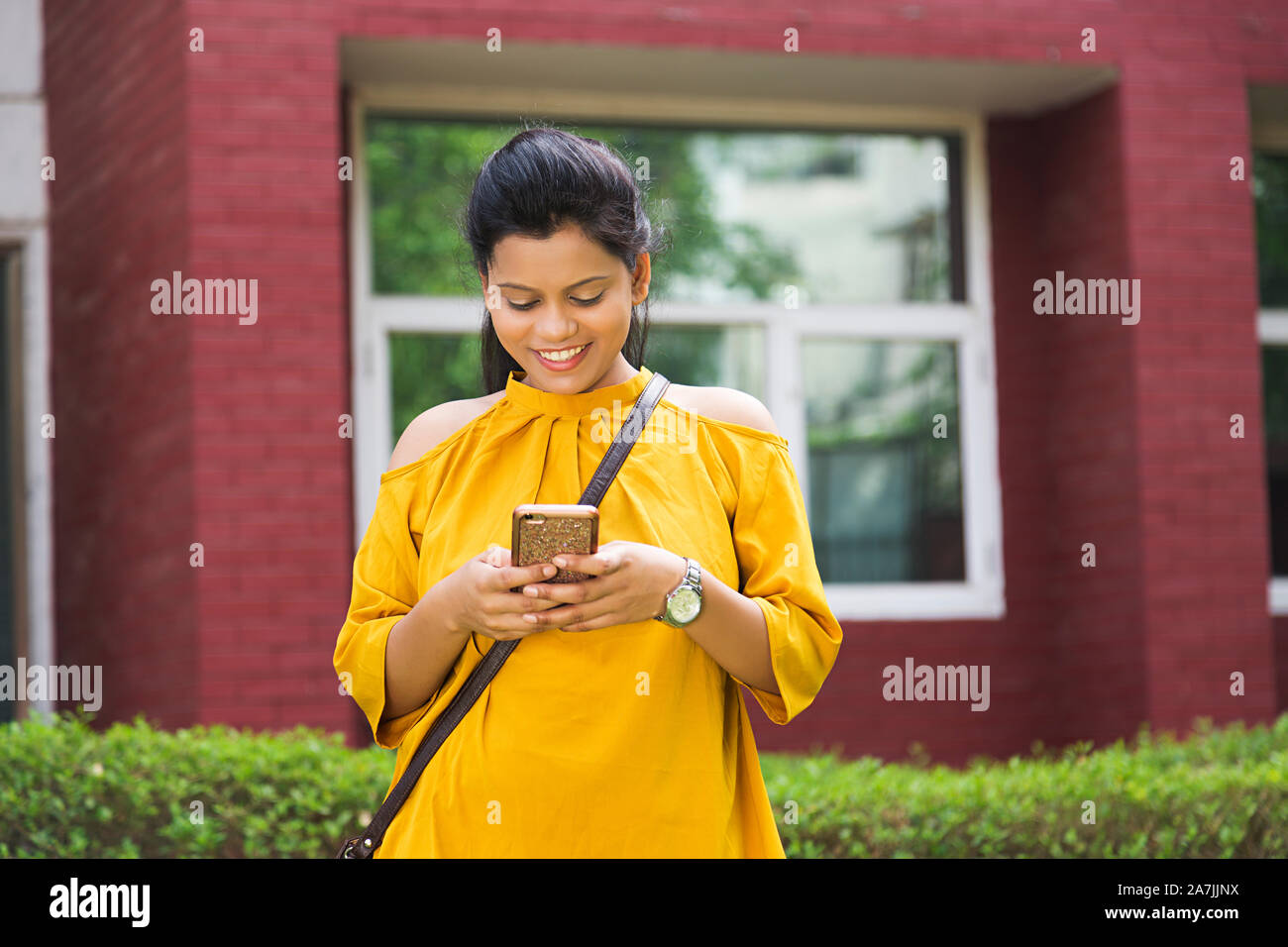 Smiling Young Female College Student Reading Text-Messaging On Cell Phone Standing In-Outside College University Campus Stock Photo
