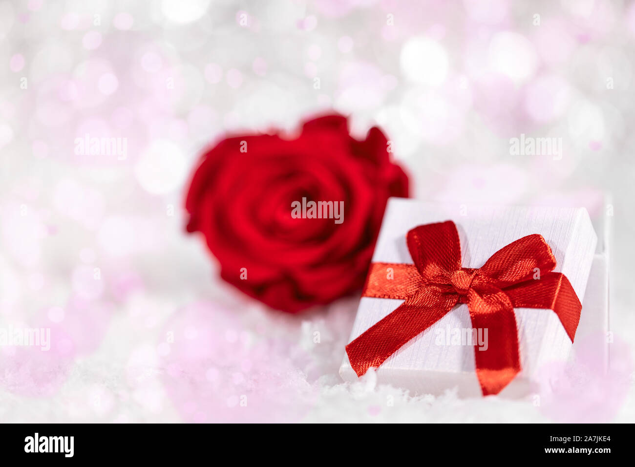 Gift box with red ribbon and rose blossom, pink and white background ...