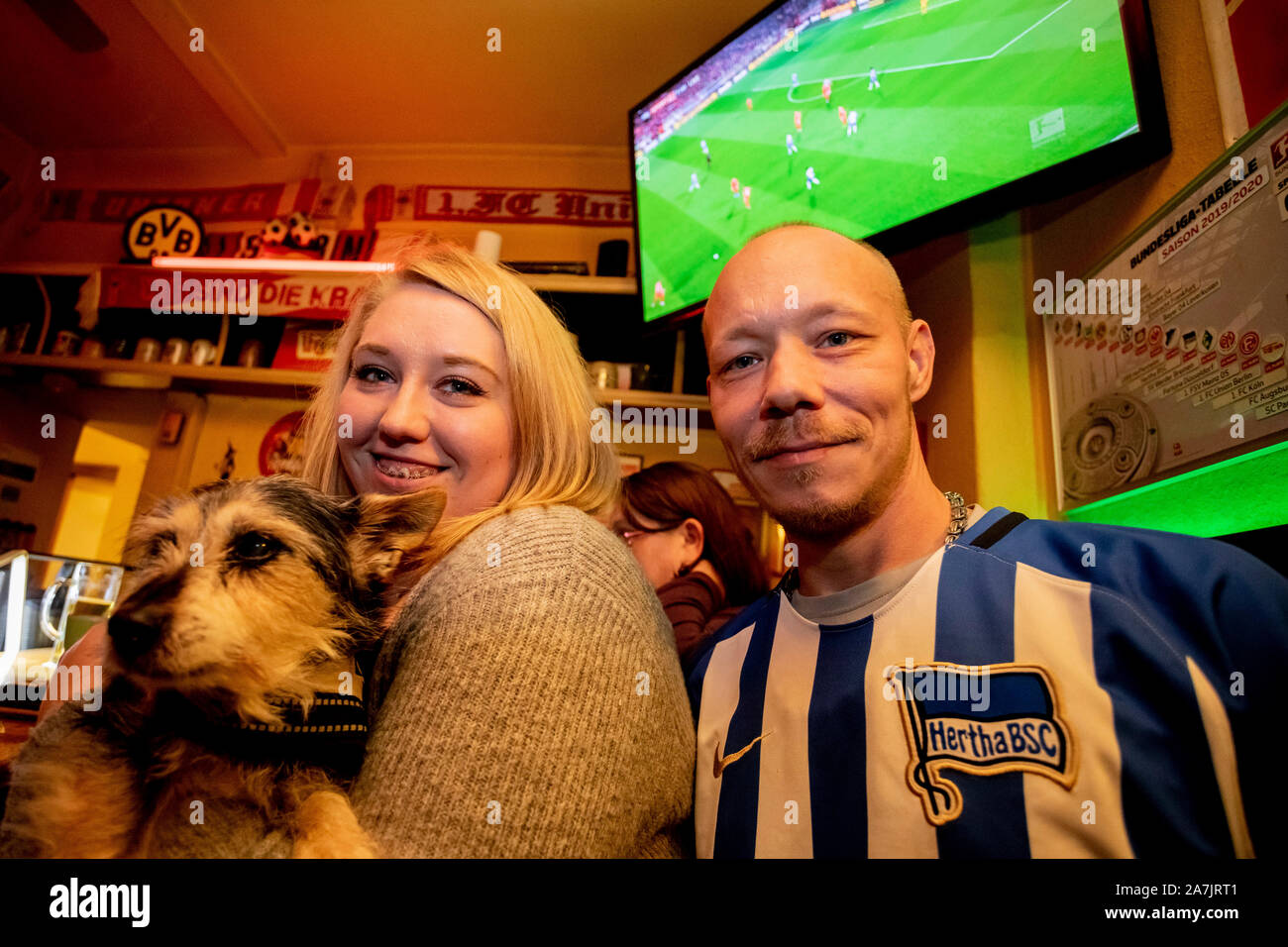 Berlin, Germany. 02nd Nov, 2019. Marcus Welk, Hertha fan, stands next to Solveig Freiberg, 'Fan-Anhang', and foster dog Tapsi during the derby between Hertha BSC and the 1st FC Union Berlin in the Kiezkneipe Schwarze Hexe in Prenzlauer Berg. (to dpa: 'Störer in Minderheit - Fans are happy about first city derby' from 03.11.2019) Credit: Christoph Soeder/dpa/Alamy Live News Stock Photo