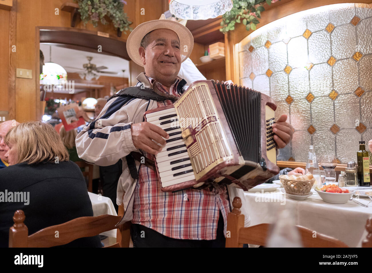 A middle aged singer accordionist in a straw hat performs for tips at a restaurant in Venice, Italy. Stock Photo