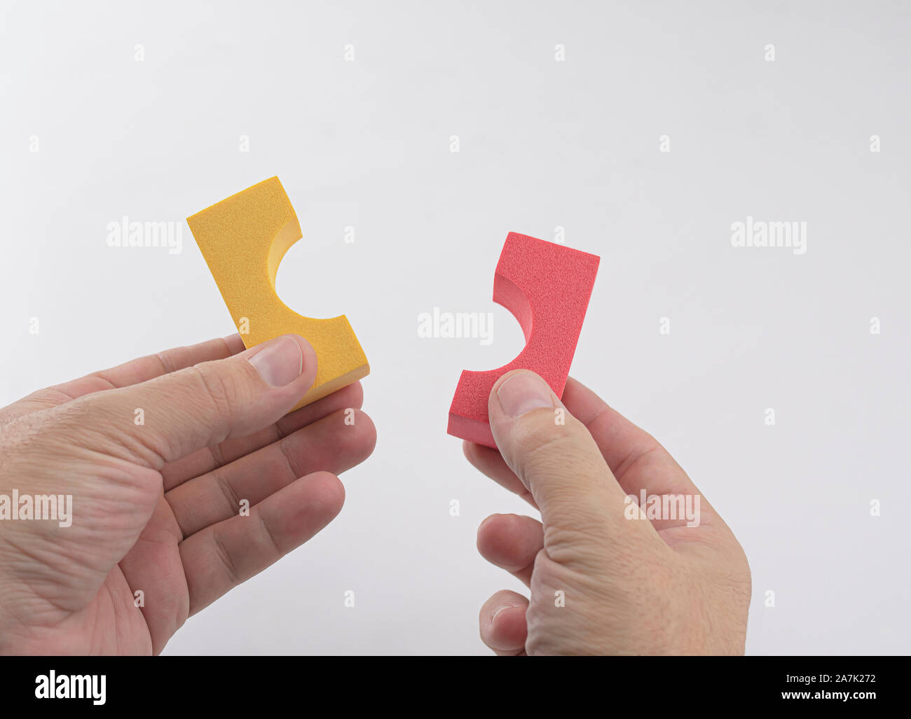Caucasian man's hands with two pieces of a foam and red and yellow children's construction toy on white background. Conceptual. Stock Photo