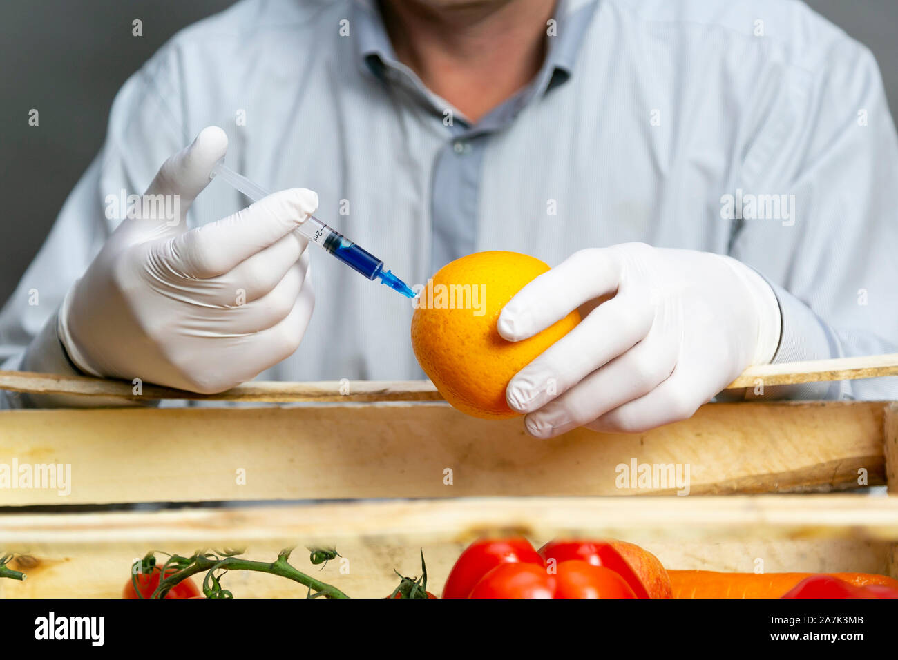 A man injects chemicals into an orange, pesticides and fertilizers and chemicals with a syringe to increase the shelf life of the fruit. Stock Photo