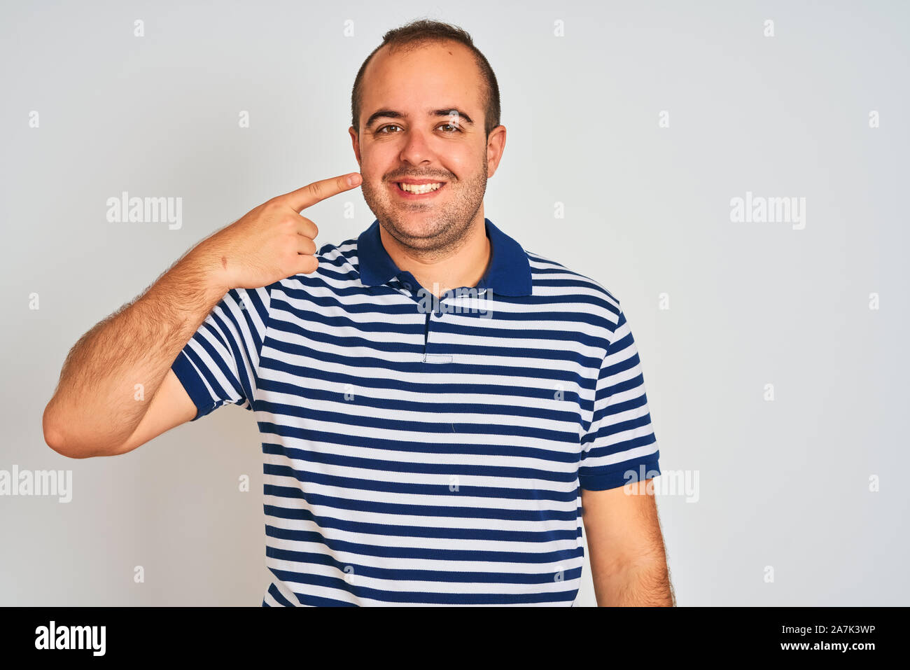 Young man wearing casual striped polo standing over isolated white  background Pointing with hand finger to face and nose, smiling cheerful.  Beauty con Stock Photo - Alamy