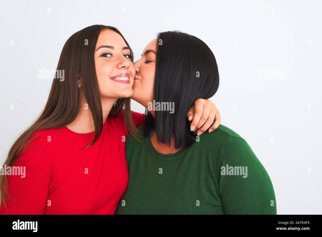 Young beautiful friends smiling happy and confident wearing casual clothes. Standing with a smile on face hugging and kissing over isolated white back Stock Photo