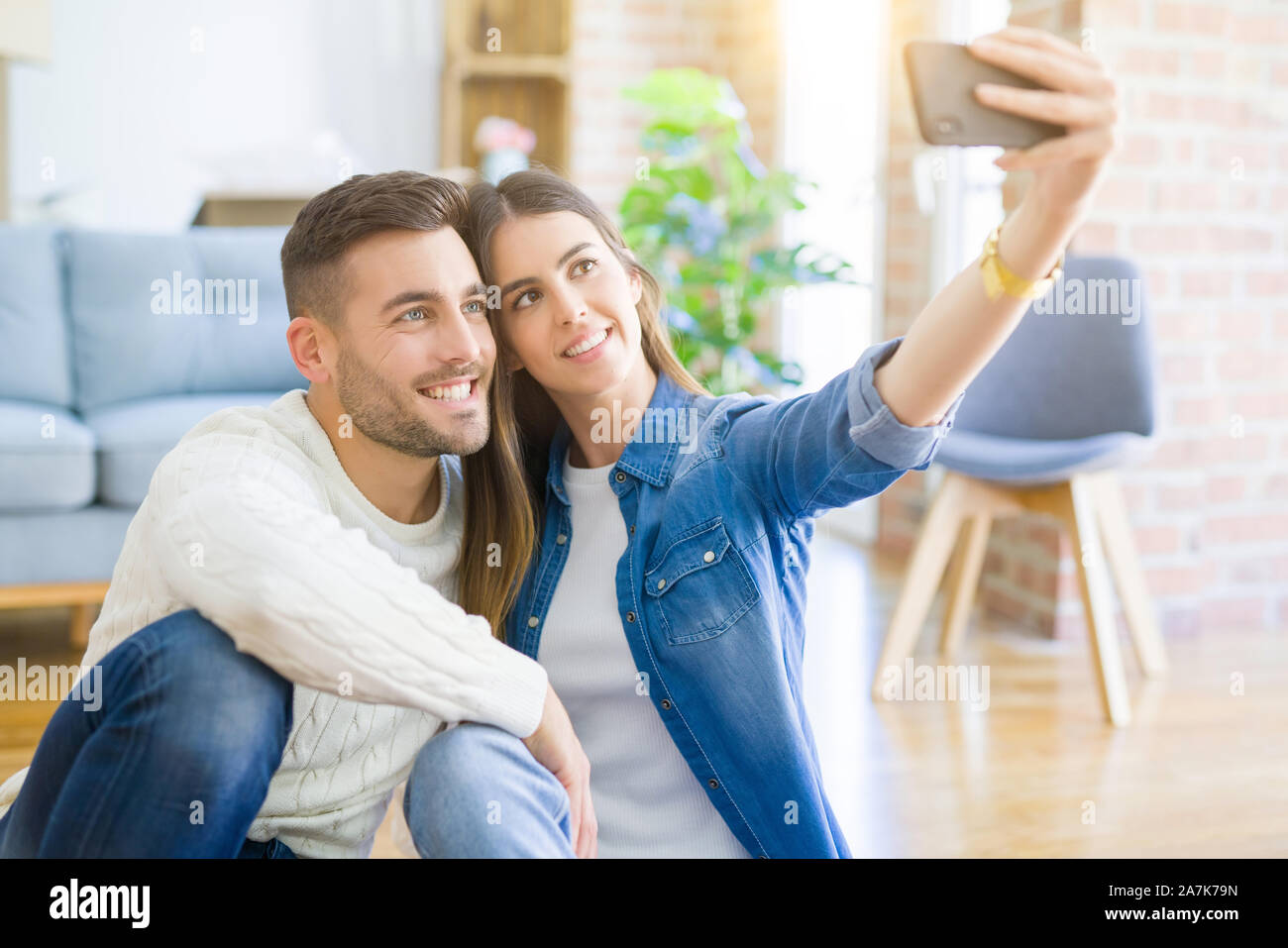 Young couple sitting on the floor of new house taking a selfie photo ...