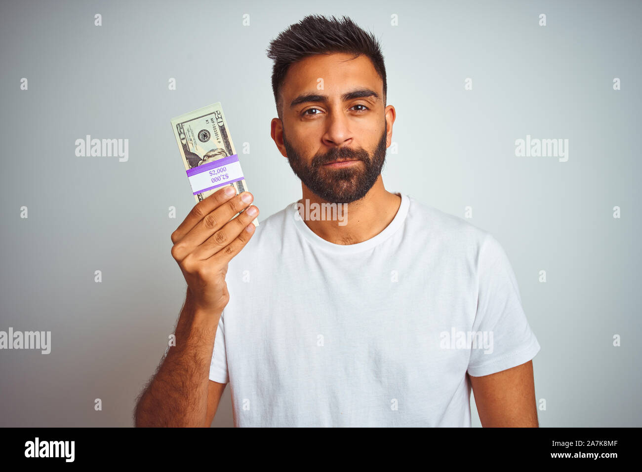 Young indian man holding dollars standing over isolated white ...