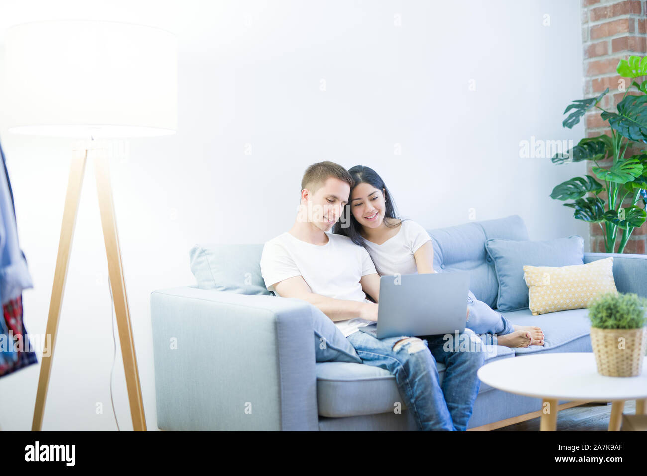 Young beautiful couple sitting on the sofa using laptop at new home ...